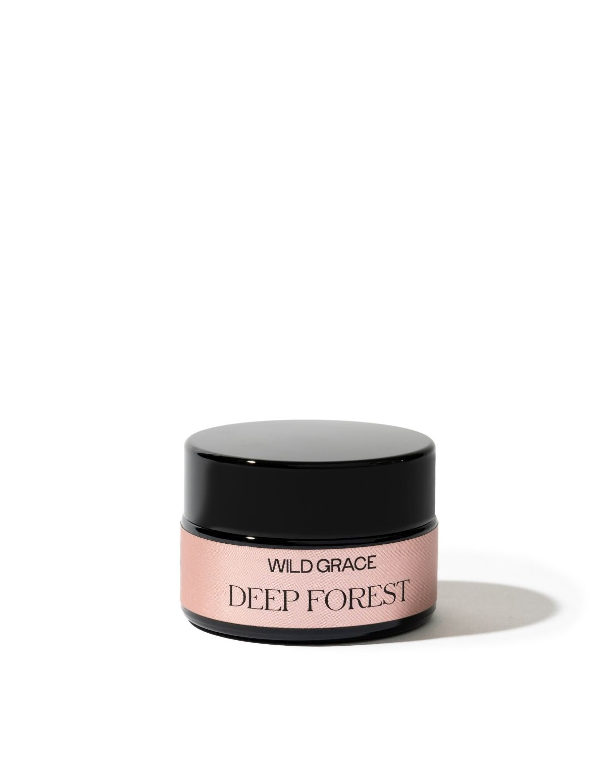 A small cosmetic jar with a glossy black lid and a pale pink label reading 'WILD GRACE DEEP FOREST' on a clean white background.