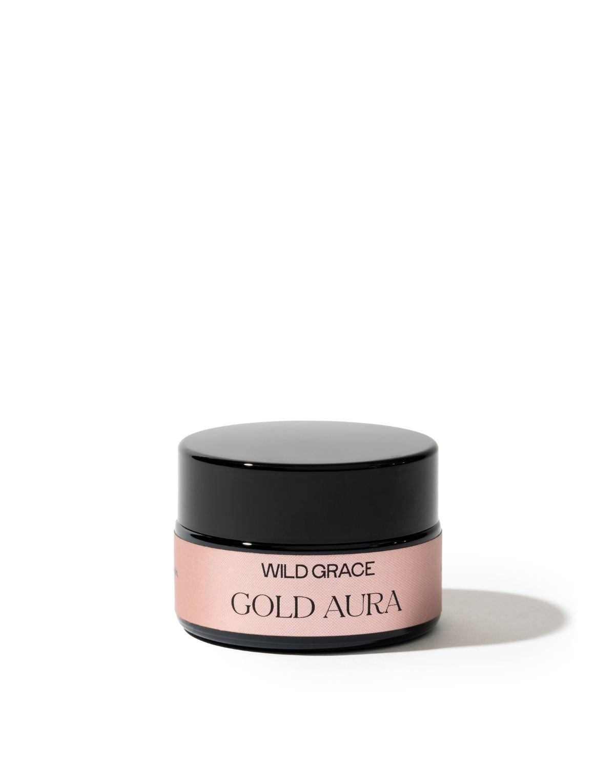 A small cosmetic jar with a glossy black lid and a dusty pink label reading 'WILD GRACE GOLD AURA' on a clean white background.