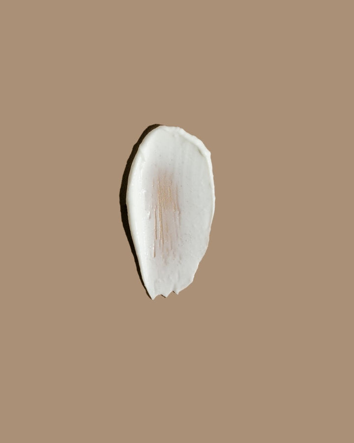 A textured swipe of white cream or makeup on a solid warm brown background.