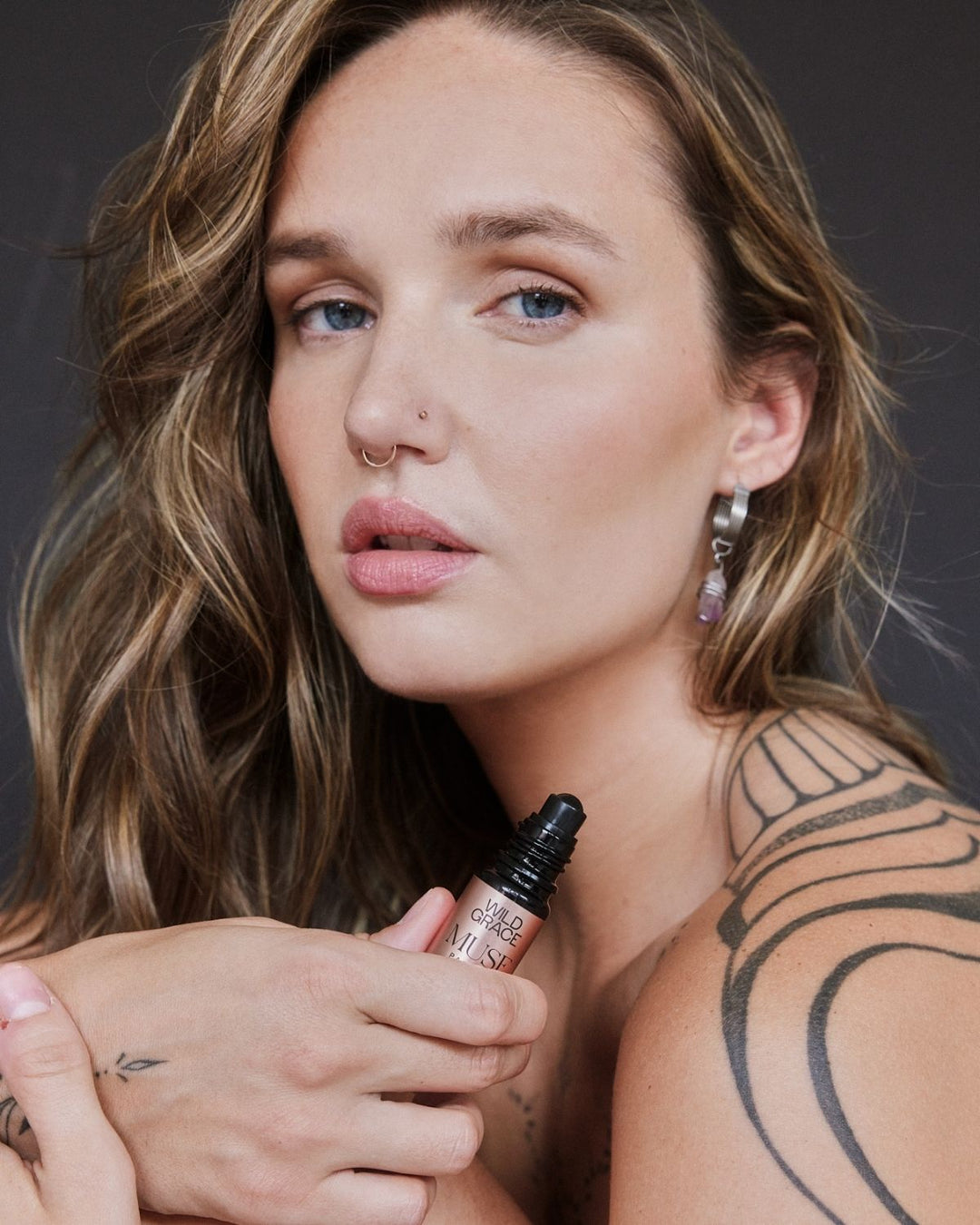 Woman holding a roll-on bottle of MUSE perfume by wild grace with a dark background