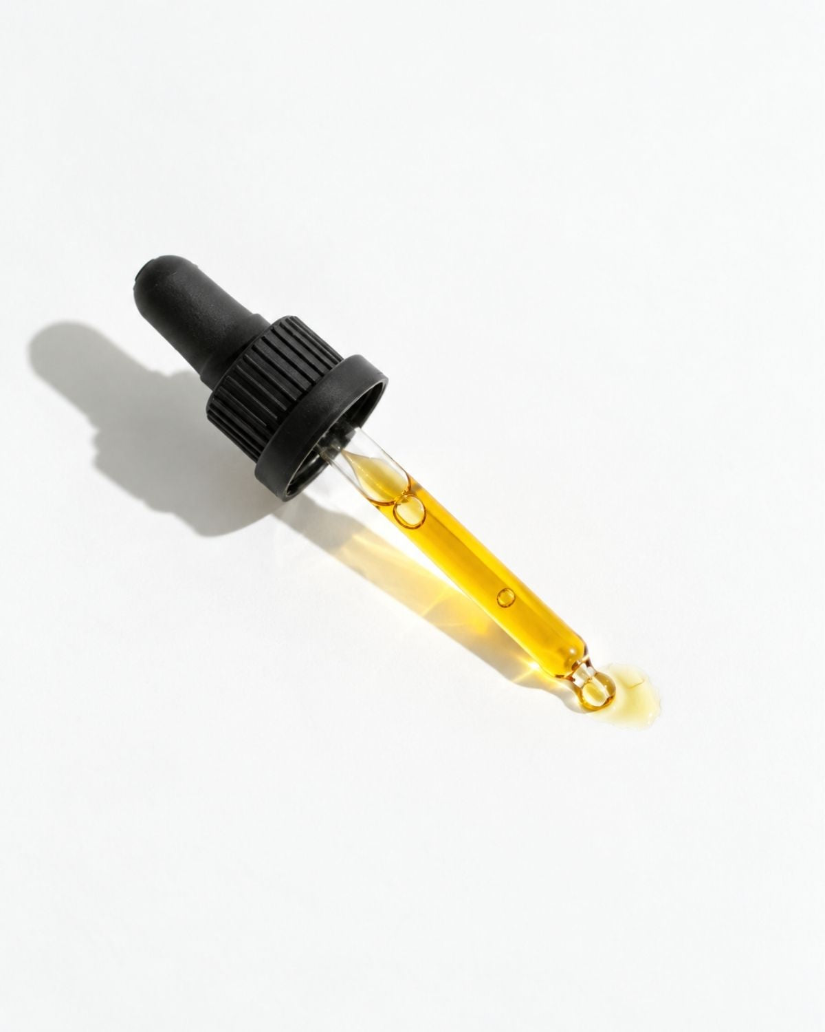 A glass dropper bottle filled with golden yellow liquid, featuring a black rubber bulb and a ribbed black cap, set against a clean white background with a soft shadow.